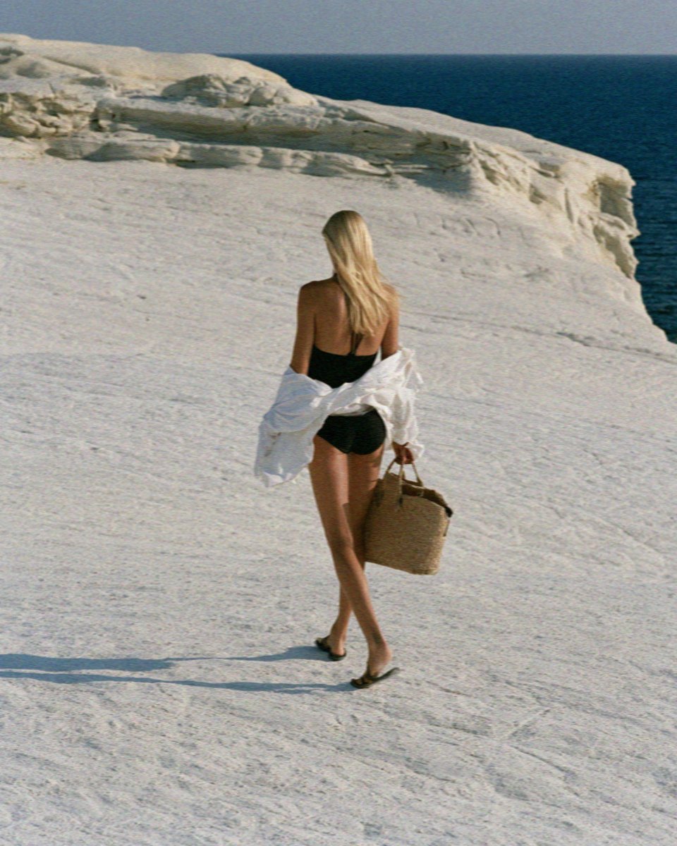 Victoria van der Berg crossing the white rock of Sarakiniko on Milos with a straw basket