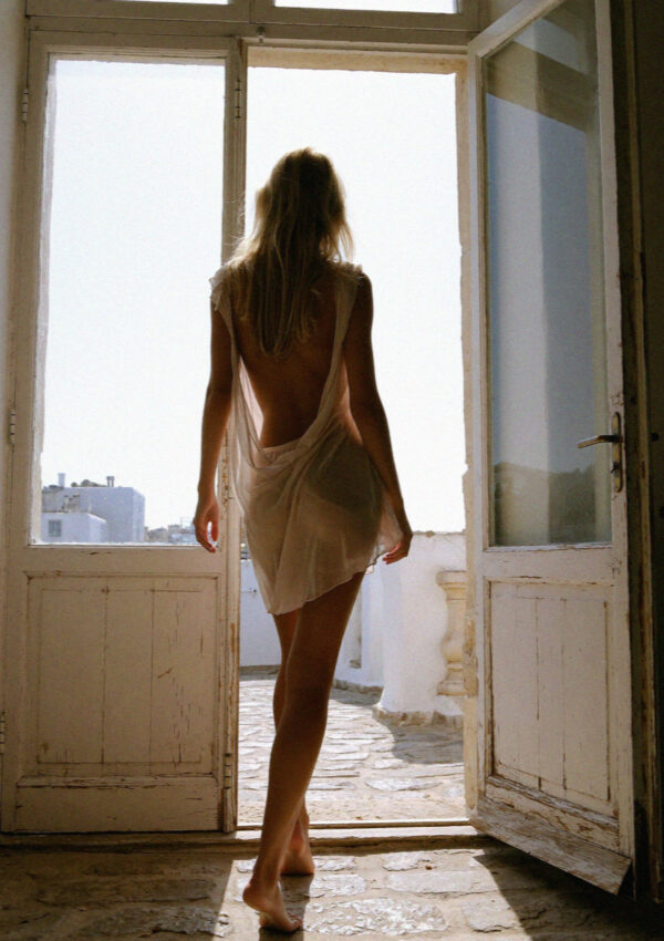 Victoria van der Berg in a slip dress backlit in an open villa doorway in the evening on Mykonos