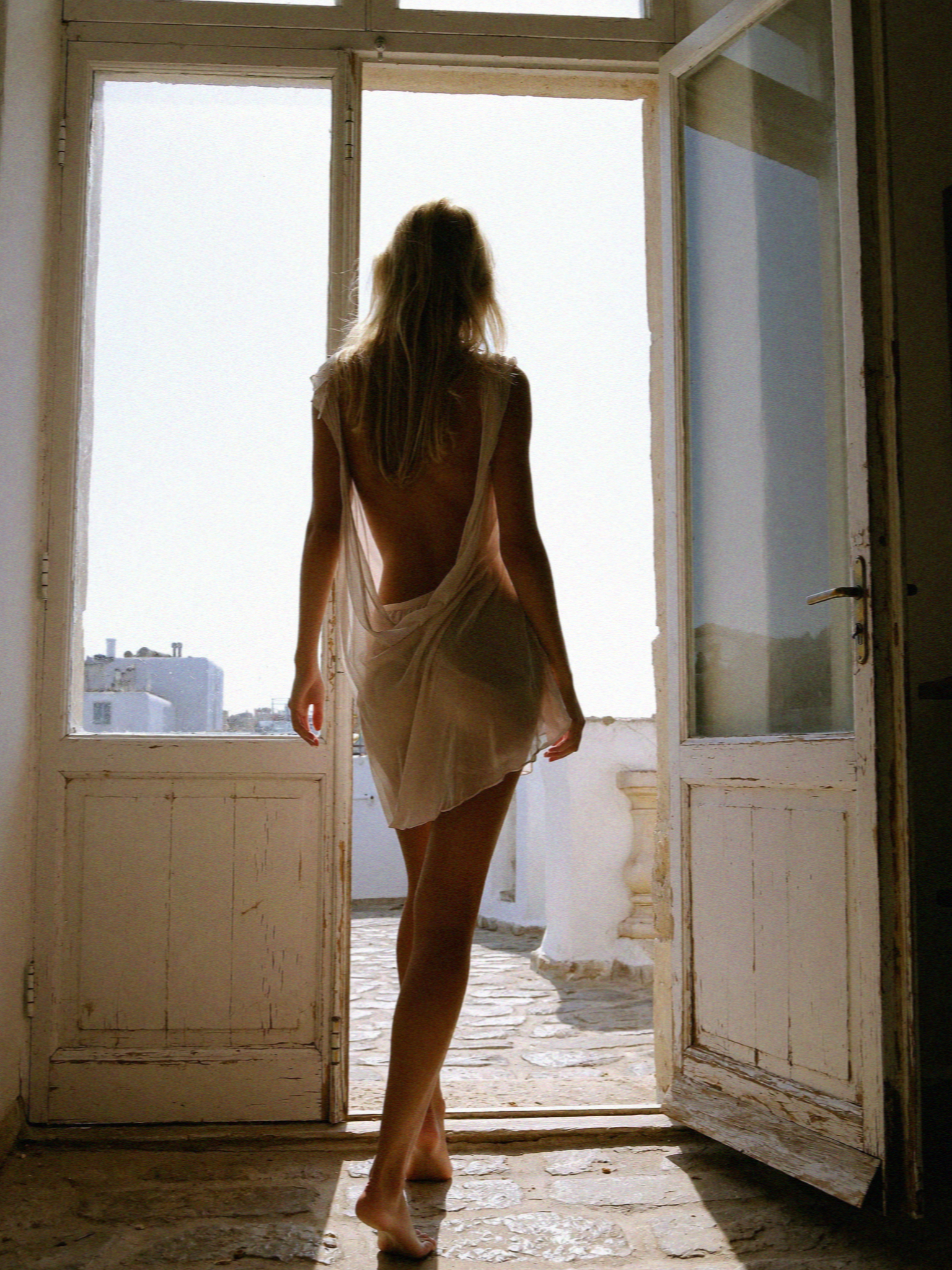 Victoria van der Berg in a slip dress backlit in an open villa doorway in the evening on Mykonos