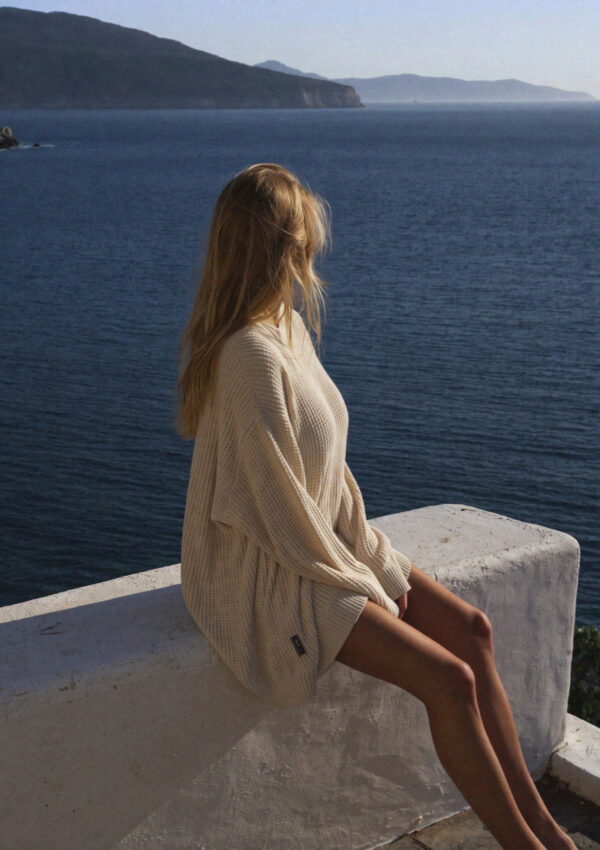 Victoria van der Berg in an oversized knit sitting on a villa wall above the sea at first light on Mykonos