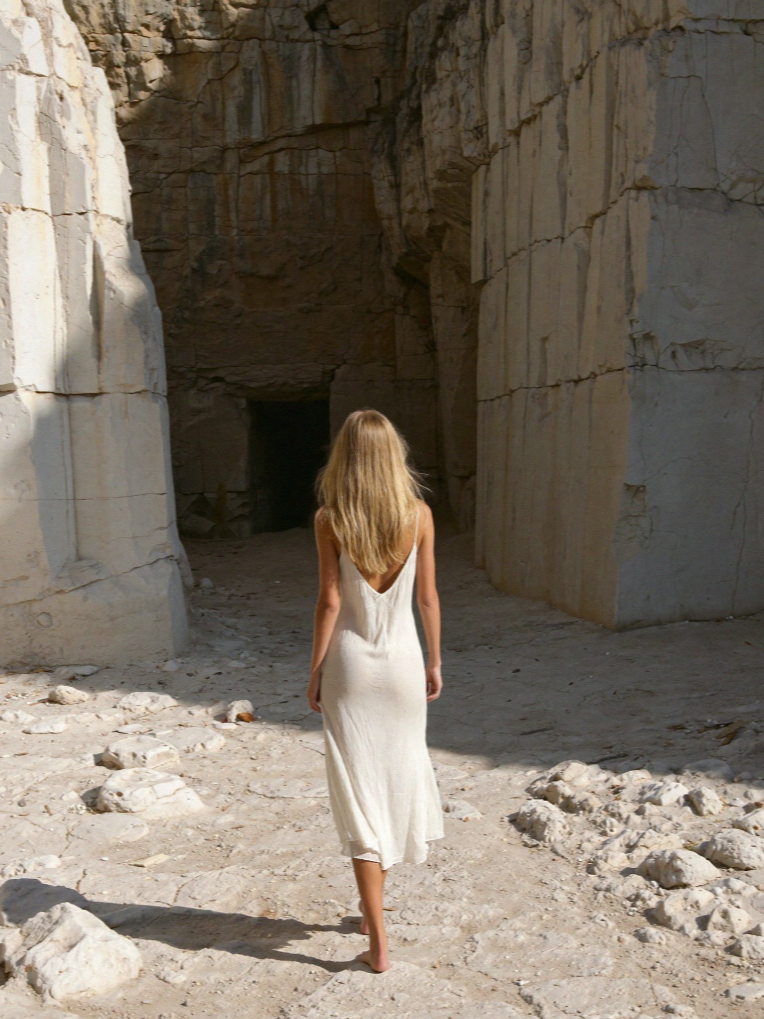 Victoria van der Berg in a white slip dress walking into an old marble quarry on Naxos