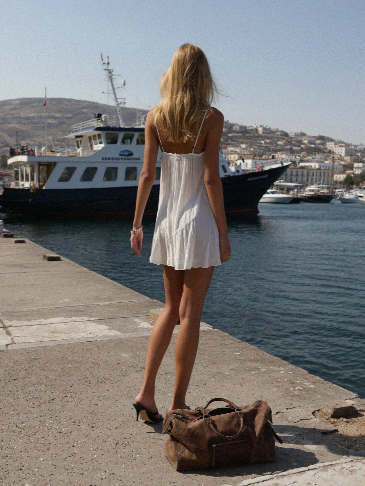 Victoria van der Berg arriving on the harbour at Parikia, Paros, with a leather holdall at her feet