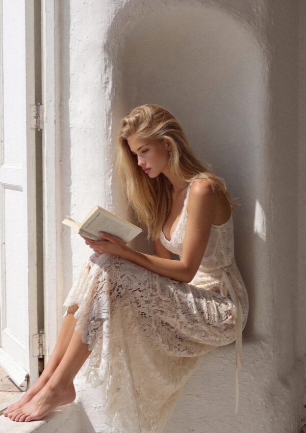 Victoria van der Berg reading barefoot in a whitewashed window niche of a cave room on Santorini